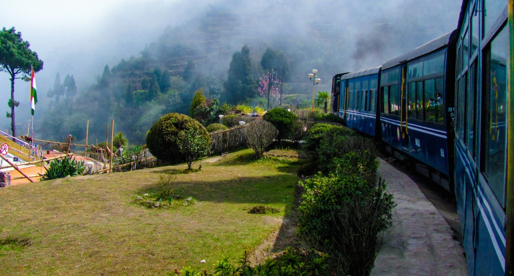 Train passing a beautiful garden and entering into fog. Surrounded by tree covered mountains copy